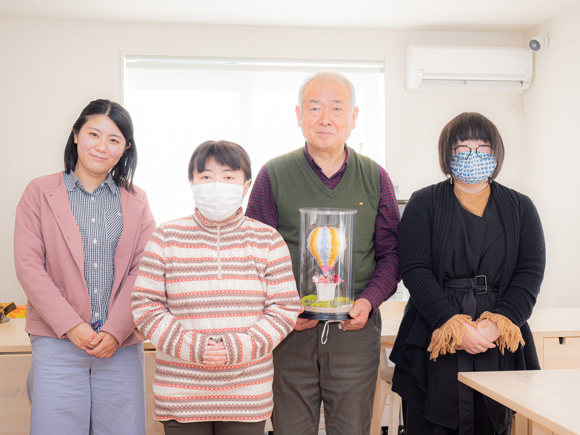 フラワーアレンジを持った田中先生とスタッフ・メンバーで記念写真
