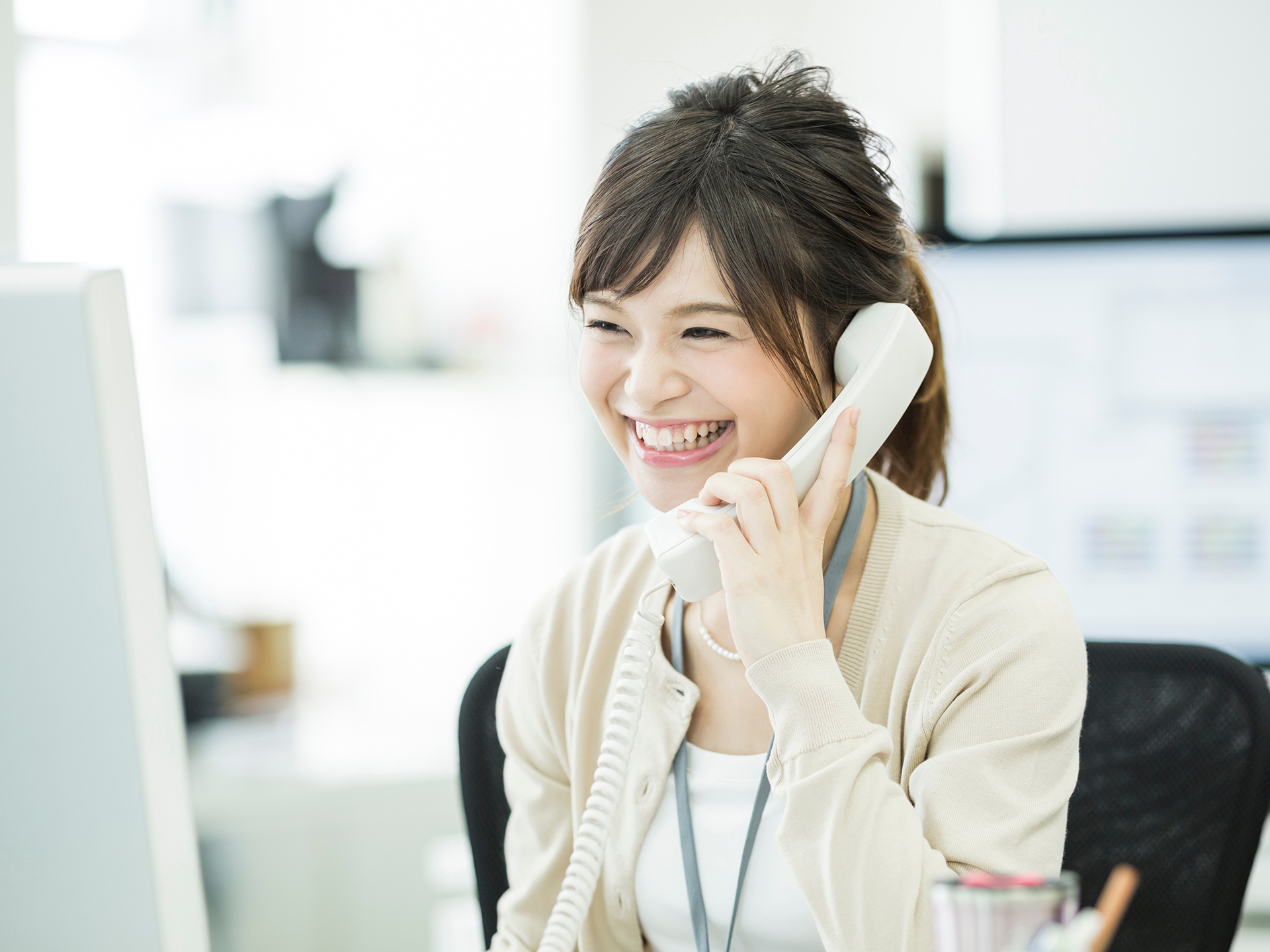 オフィスで笑顔で電話する女性の写真｜AdobeStock